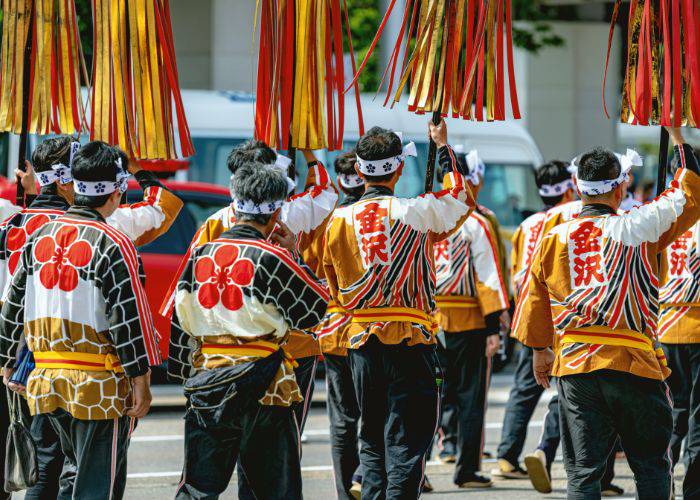 The bright reds and yellows of the Kanazawa Hyakumangoku Festival in Ishikawa as men parade down the street with banners.